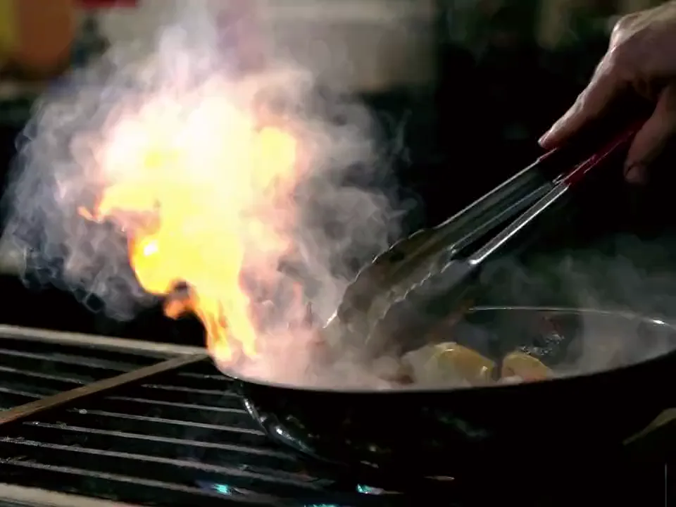 A flame rises from a pan on the stove as a participant stirs, in a cooking class at the studio