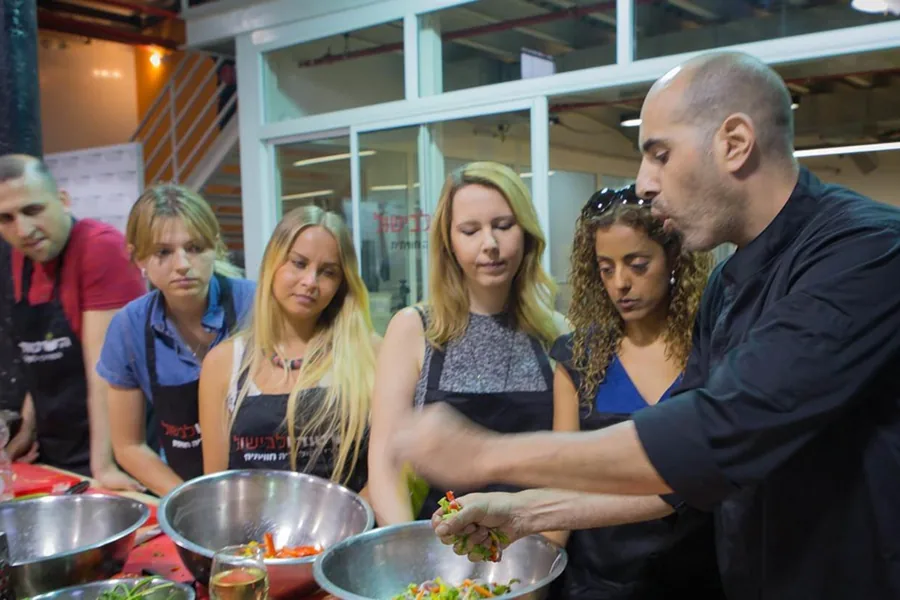 A chef explains to a group over a casserole at the workstation